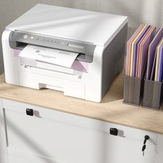 a white printer sitting on top of a counter next to some papers and pen holders