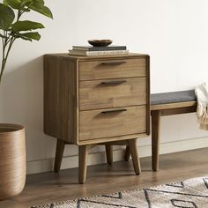 a wooden cabinet with two drawers next to a bench and potted plant on the floor