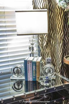 a lamp sitting on top of a glass table next to a window covered in blinds