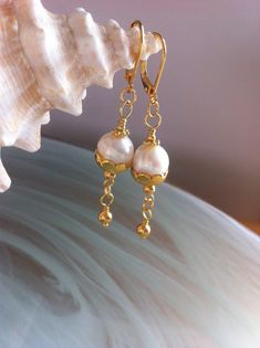 In a minimalist style, a freshwater pearl in a gold-plated scalloped cup and a suspended golden pearl. Gold earrings composed of 9.5 mm freshwater pearls in a 10 mm scalloped cup. A gold-plated bead is suspended. Gold plated back lever earrings. They measure 5.5 cm or 2 and a quarter inches, 2 and a quarter inches from the top of the hooks to the bottom. Earrings with quality freshwater pearls in a minimalist design but with chic that you can wear in a formal evening or every day, plus the delivery is free. Pearl Gold Earrings, Earring Pearl, Gold Filigree Earrings, Mystic Topaz Earrings, Golden Pearl, Cobalt Blue Earrings, Native American Beaded Earrings, Gold Leaf Earrings, Womens Earrings Studs