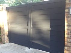 an image of a driveway gate that has been painted dark gray and is in front of a brick building