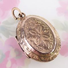 Ornately engraved floral motif designs decorate both sides of this antique 10k solid yellow gold locket pendant. The fully engraved floral reversible pendant features detailed linework, scrolling and floral details, which differs on each side. The locket opens with the help of two tiny knobs and closes securely with a light snap. Inside you will find both original frames attached to glass inserts. The locket tested as 10k gold in three locations (no hallmark). The large added bail at top is gold filled. This antique lovingly aged piece is in very good condition for its turn-of-the-century age. It has some expected surface wear and a few tiny dings to its outer shell. There are two dark lines where the trim was joined on each panel. Please see photos for condition and detailed measurements