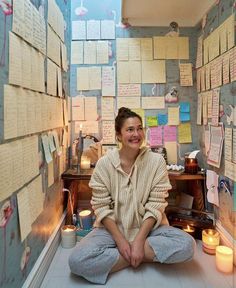 a woman sitting on the floor in front of a wall full of notes and candles