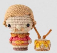 a small crocheted doll holding a tiny toy drum and wearing a knitted hat