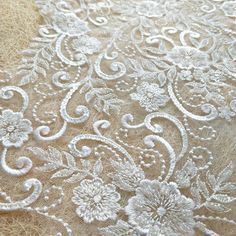 an embroidered fabric with white flowers and leaves on the bottom, is shown in close up