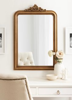 a mirror sitting on top of a white desk next to a vase with flowers in it