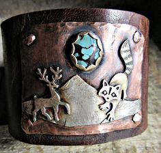 Into the Wild Distressed Wide Leather Cuff bracelet by Weathered Soul Jewelry, raccoon, artisan made, rustic, Buck, Deer, Antlers, OOAK, USA This is truly and amazing piece. It is wide Buffalo hide distressed leather with 2 heavy duty bronze snaps set for a 7 inch wrist size. Keep in mind they fit a little snugger than usual with wide leather so this could fit a tad smaller wrist still. Genuine turquoise matrix stone set in silver on copper. Raccoon and Deer are sterling as well as the mountains Unique Hand Forged Cuff Bracelet, Artisan Hand Forged Adjustable Cuff Bracelet, Rustic Handmade Cuff Bangle Bracelet, Handmade Rustic Style Bangle Jewelry, Handmade Rustic Bangle Jewelry, Rustic Handmade Bangle Jewelry, Rustic Stamped Cuff Bracelet Gift, Rustic Brown Cuff Bracelet As Gift, Rustic Brown Cuff Bracelet Gift