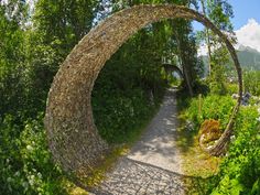 an arch made out of rocks in the middle of a path surrounded by greenery