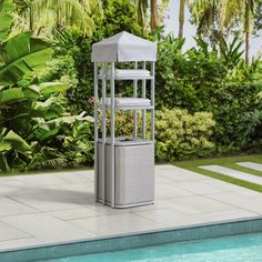 a white birdcage next to a swimming pool with plants and trees in the background