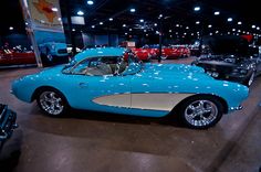 an old blue car is on display in a showroom with other cars and people looking at it