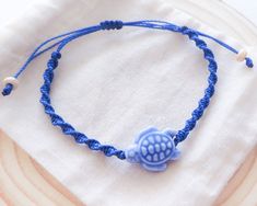 a blue string bracelet with a small turtle bead on it's end, sitting on top of a white cloth