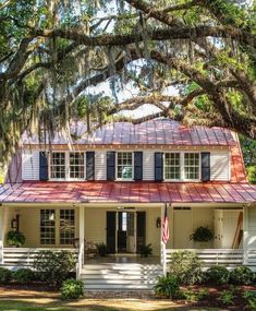 a white house with red roof and blue shutters on the front porch, surrounded by trees