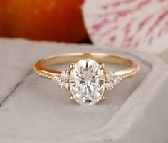 an engagement ring with three stones on it, sitting in front of an orange piece of fruit