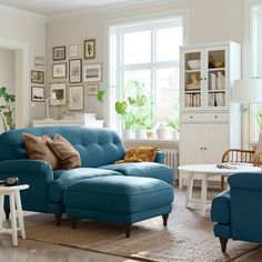 a living room with blue couches and white tables in the corner, along with pictures on the wall