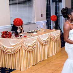 a bride and groom standing next to each other in front of a table with red flowers