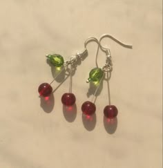 three red and green glass beads hanging from silver earwires on a white surface