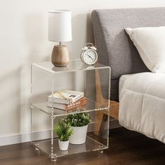 a glass shelf with a clock on it next to a bed and nightstand in a bedroom