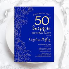 a blue and gold 50th surprise birthday party card on a white plate with silver ribbon