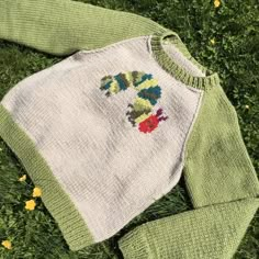 a knitted sweater laying on top of green grass with flowers in the back ground