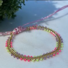 a close up of a beaded bracelet on a table with flowers in the background