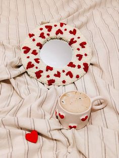 a cup of coffee sitting on top of a bed next to a heart shaped wreath