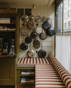 pots and pans are hanging on the wall above a bench in a kitchen with striped cushions