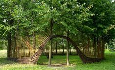 a sculpture made out of branches in the middle of a field with trees around it