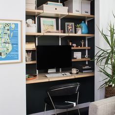 a desk with a computer on top of it next to a chair and potted plant