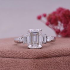 an emerald - cut diamond ring with three baguettes sits on top of a pink blanket