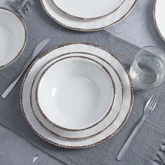 the table is set with white dishes and silver cutlery, which are on top of a gray placemat