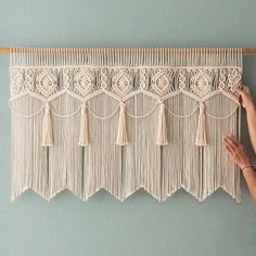 a woman is working on a macrame wall hanging with white yarn and tassels