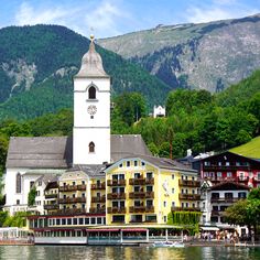 a white and yellow building sitting on the side of a river next to a lush green hillside