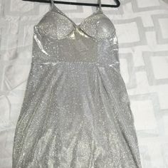 a silver dress hanging on a hanger next to a white bed sheet with an open back