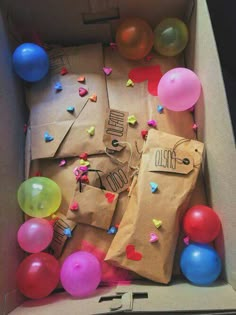 an open cardboard box with balloons and confetti on the inside, including a brown paper bag