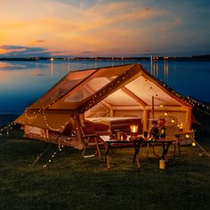 a tent is set up on the grass by the water at night with string lights strung around it