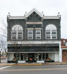 an old black and white building on the corner of a street with trees in front of it