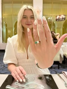 a woman sitting at a table holding her hand up to the camera with two rings on it