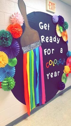 a colorful classroom door decorated with paper flowers and a paint brush that says get ready for a colorful year