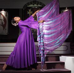 a woman in a purple dress is standing on some steps and holding a scarf over her head