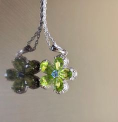 DeKara Designs Silver Metal- Sterling Silver, .925. Stones- 5 Natural Pear Shape Peridot 5 Carats, 1 Round Natural Blue Topaz, 5 Diamonds G-H Color SI2 Clarity 0.02 Carats. Measurements- Necklace is 18 Inches Long. Pendant is Bit Over An Inch Long Including Bail. Beautifully handmade Art Deco inspired halo diamond blue topaz peridot necklace made in sterling silver. There are five natural beautiful green pear shape peridot stones that are all professionally prong set. There is a prong set round Fine Jewelry Lime Green Birthstone, Peridot Jewelry With Gemstone Accents For May Birthstone, Fine Jewelry In Green Peridot, Fine Jewelry Lime Green Gemstone, Peridot Gemstone Jewelry For May Birthstone, Green Peridot Fine Jewelry, Fine Green Peridot Jewelry, Green Sterling Silver Flower Pendant Jewelry, Fine Jewelry Peridot Necklace For Anniversary