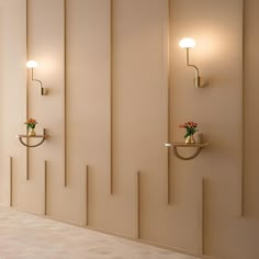 two wall lights on the side of a white wall next to a vase with flowers