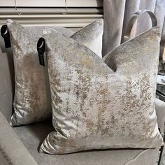 two silver pillows sitting on top of a gray couch