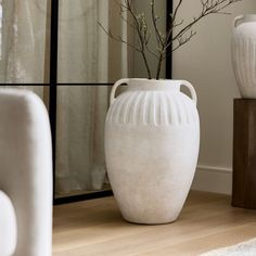 a white vase sitting on top of a wooden table next to a mirror and chair