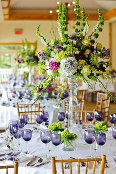 an arrangement of flowers and greenery is displayed in the center of this table setting