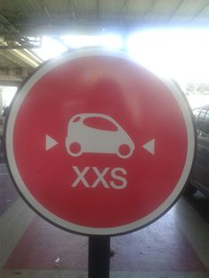 a red and white sign that says xxs next to some cars in a parking garage