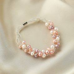 a bracelet with pink and white pearls is on top of a satin material surface,