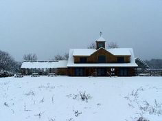 a large house covered in snow next to a field filled with grass and trees on a cloudy day