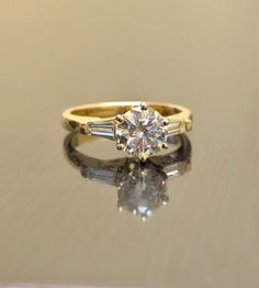 DeKara Designs Collection An Elegant Yellow Gold Diamond Engagement Ring, Modern, Tasteful, Timeless and Affordable. Metal- 18K Yellow Gold, .750. Stone- Center Round Diamond J-K Color SI2 Clarity 1.01 Carats, 2 Baguette Diamonds H Color VS2 Clarity 0.20 Carats. Size- 6. FREE SIZING Beautiful Diamond Engagement Ring Handmade in 18K Yellow Gold. The ring features a fiery round diamond in the center that is professionally set in between six prongs in 18K white gold. There is one channel set baguet Fine Jewelry For Marriage With Brilliant Cut, Timeless Gia Certified Rings, Heirloom Yellow Gold Wedding Ring, Yellow Gold Solitaire Baguette Cut Wedding Ring, Timeless Gold Diamond Wedding Ring, 14k Gold Diamond Ring With Prong Setting For Marriage, Elegant Gold Diamond Ring With Classic Cut, Elegant Gold Diamond Ring Classic Cut, Classic Yellow Gold Diamond Ring For Wedding