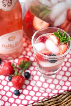 two glasses filled with ice and strawberries on a table next to bottles of wine