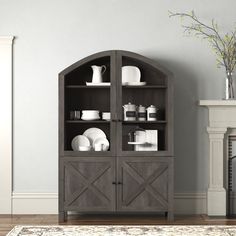 a wooden hutch with dishes on it in front of a fireplace